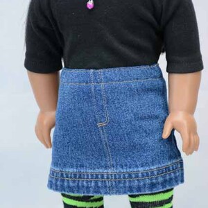 Puede incluir: Una mu&ntilde;eca con una camisa negra de manga corta, una falda vaquera y medias de rayas de colores. La mu&ntilde;eca lleva un collar de cadena plateada con un colgante de coraz&oacute;n rosa.