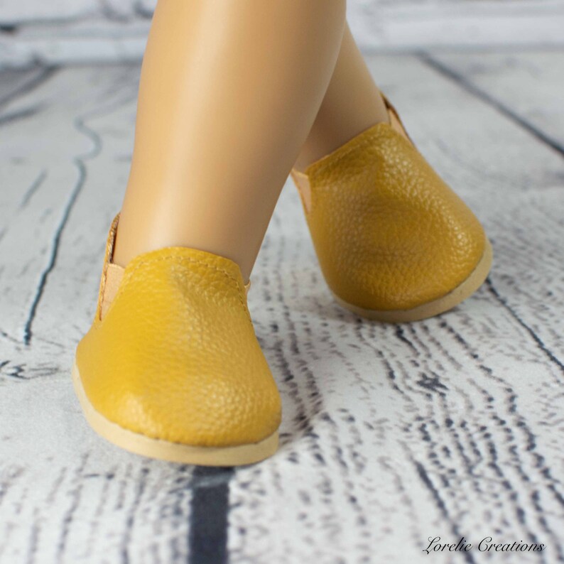 Puede incluir: Un par de zapatos amarillos de cuero para una mu&ntilde;eca. Los zapatos tienen un dise&ntilde;o sencillo y est&aacute;n hechos de un cuero suave y flexible.