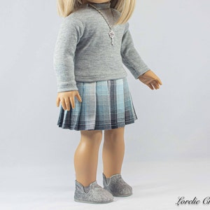 May include: A gray long-sleeved shirt with a silver key necklace and a blue and white plaid skirt. The doll is wearing gray shoes.