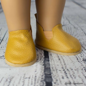 Puede incluir: Un par de zapatos amarillos de deslizamiento con un acabado de cuero texturizado. Los zapatos tienen una suela marr&oacute;n claro y una ligera banda el&aacute;stica en la parte superior.
