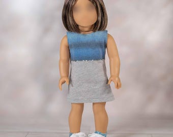 May include: A doll wearing a sleeveless dress with a blue and gray color block design. The top of the dress is blue, fading into gray, with a line of small, silver embellishments. The doll is also wearing blue glitter sneakers with white laces.