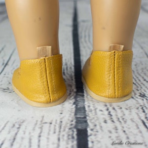 Puede incluir: Un par de zapatos amarillos de cuero con deslizamiento con correas el&aacute;sticas en la parte posterior. Los zapatos est&aacute;n sobre una superficie de madera.