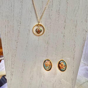 May include: A gold necklace with a heart-shaped pendant and matching earrings. The pendant and earrings feature a blue and gold design.