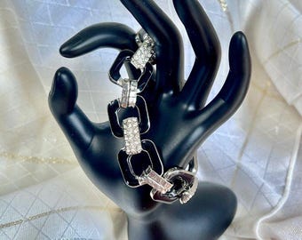 May include: A black and silver bracelet with a chain link design. The bracelet features rectangular black links with silver accents and sparkling clear stones. The bracelet is displayed on a black hand.