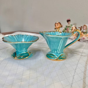 May include: A turquoise creamer and sugar bowl set with gold trim. The creamer has a handle and the sugar bowl has a scalloped edge.