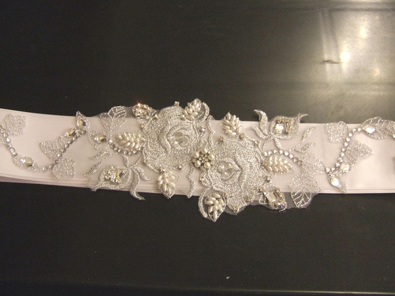 May include: A white satin bridal sash with silver floral embroidery and rhinestones.