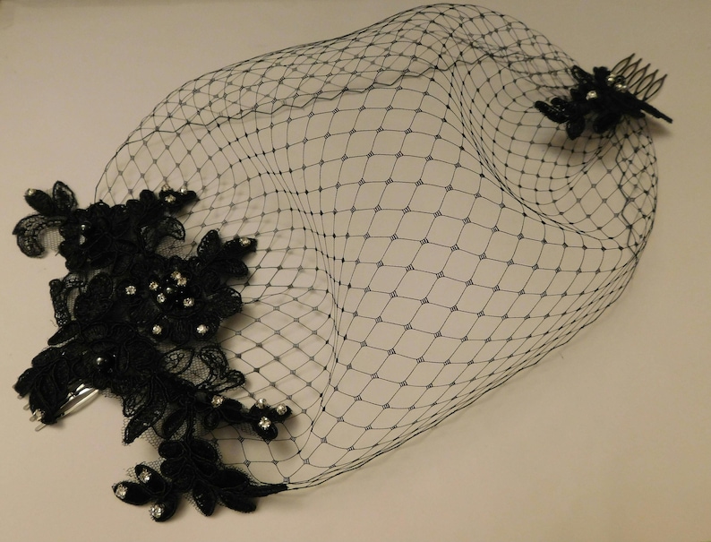 black birdcage veil with a delicate floral lace design and a comb for attaching to hair. The veil is made of fine netting and has a soft, flowing shape.