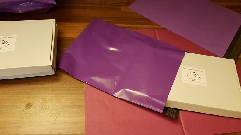 May include: Two white boxes with the text "The Dragon - Bead Alchemy" and a black and white illustration of a dragon. The boxes are wrapped in a purple poly mailer.