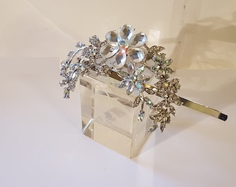 May include: A silver hair comb with a floral design featuring clear iridescent rhinestones. The comb has a long, thin handle.