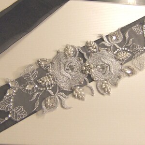 May include: A black satin ribbon with silver embroidery and rhinestones, featuring a floral design with two large roses. The ribbon is perfect for adding a touch of elegance to any occasion.
