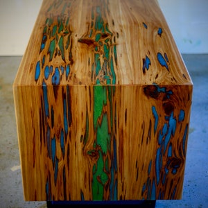 May include: A wooden cube table with a natural wood finish and blue and green resin accents. The table has a unique, organic look and is perfect for a modern home.