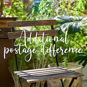 May include: A wooden chair with a black metal frame is positioned in front of lush greenery. The chair has a slatted seat and backrest. The text "Additional postage difference" is written in a cursive font across the chair.