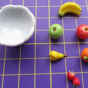 May include: A white, scalloped-edge bowl next to miniature fruit figurines. The fruit includes a yellow banana, green apple, red apple, yellow pear, orange, and two red strawberries. The fruit is arranged on a purple grid.