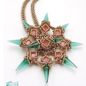 Könnte beinhalten: Eine handgefertigte Halskette mit einem sternförmigen Anhänger und einer goldfarbenen Kette. Der Anhänger hat rosa und goldfarbene Perlenarbeiten mit türkisfarbenen Glasstacheln. Das Wort "Shuriken" steht in türkisfarbener Schrift über dem Anhänger. Der Name der Designerin, Claudia Schumann, ist ebenfalls sichtbar.