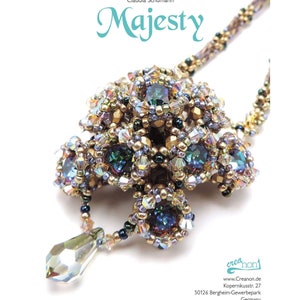 May include: A gold and silver beaded necklace with a large, multi-faceted crystal pendant. The pendant is made up of many smaller crystals and beads, and it has a teardrop shape. The necklace is called "Majesty" and is by Crea non.