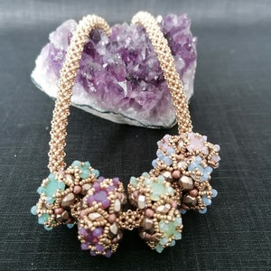 May include: A gold beaded necklace with a chain-like design and four colourful beaded clusters. The clusters are made of various shades of pink, purple, green, and blue beads.