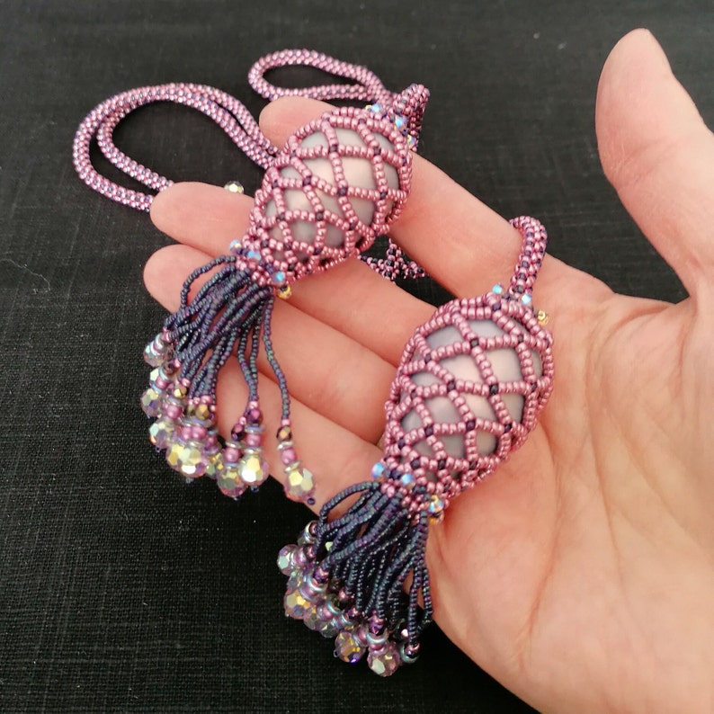 May include: A pair of beaded necklaces with pink and purple iridescent glass beads. Each necklace features a large, beaded, cage-like pendant with a tassel.