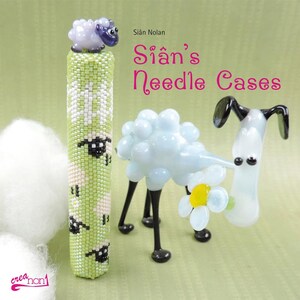 May include: A green and white beaded needle case with a small purple sheep on top. The case is decorated with a pattern of sheep and flowers. The text "Si&aacute;n's Needle Cases" is written in pink letters on a green background.