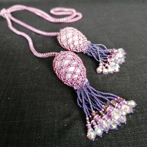 May include: A beaded necklace with two pink and purple beaded tassels. The tassels are made of small beads and have a delicate, feminine look.