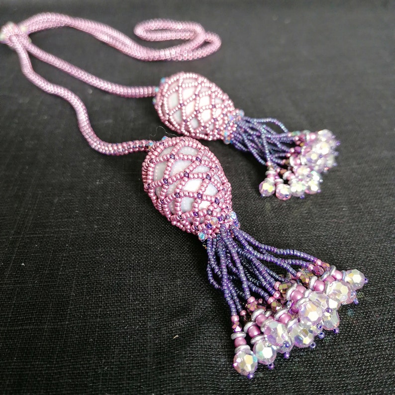 May include: A beaded necklace with two pink and purple beaded tassels. The tassels are made of small beads and have a delicate, feminine look.
