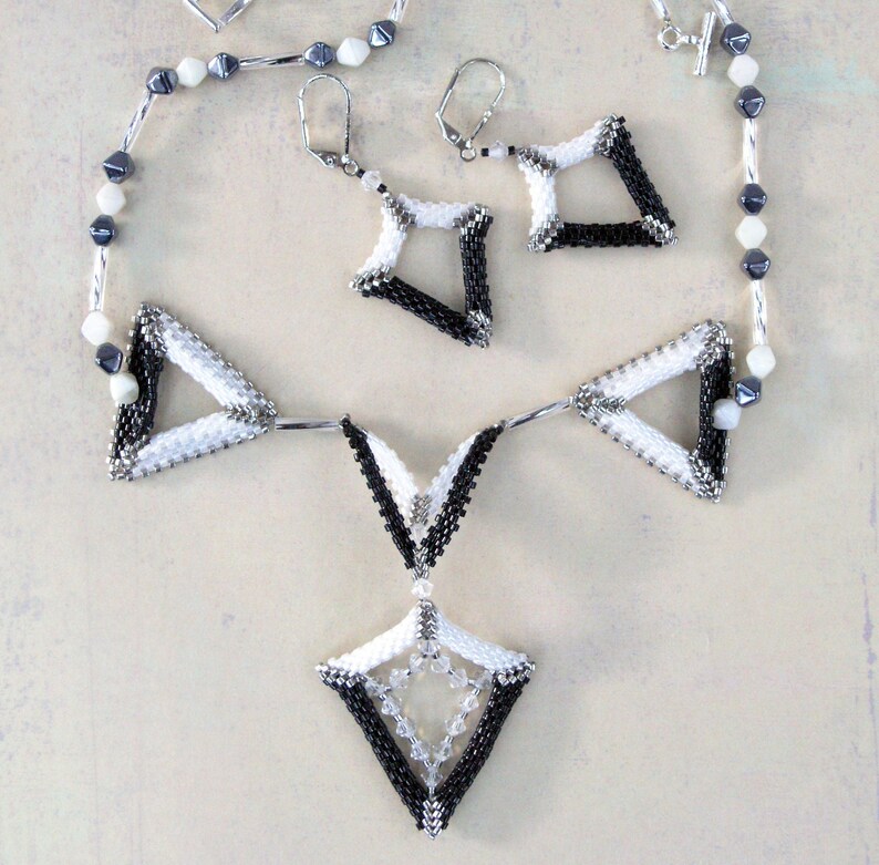 Puede incluir: Un collar de cuentas blanco y negro con un colgante geom&eacute;trico y pendientes a juego. El collar presenta una cadena larga con cuentas blancas y negras y un colgante triangular grande con un colgante m&aacute;s peque&ntilde;o en forma de diamante que cuelga de &eacute;l. Los pendientes son peque&ntilde;os y presentan un dise&ntilde;o geom&eacute;trico.