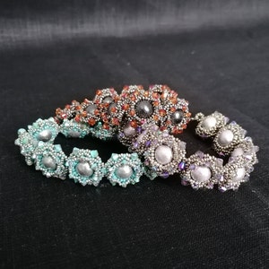 Könnte beinhalten: Drei Perlenarmbänder in den Farben Türkis, Silber und Orange. Jedes Armband hat ein sich wiederholendes Muster aus blütenförmigen Perlen mit einer zentralen Perle.