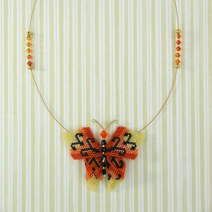 Puede incluir: Un collar de cadena dorada con un colgante de mariposa de cuentas. La mariposa es naranja, amarilla y negra con un dise&ntilde;o detallado.