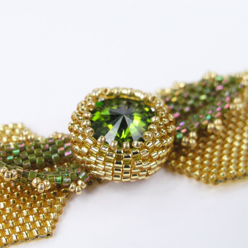 Puede incluir: Un collar de cuentas doradas con un colgante de piedra preciosa verde. Las cuentas est&aacute;n dispuestas en un patr&oacute;n geom&eacute;trico, creando un dise&ntilde;o delicado e intrincado.