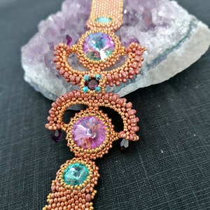 Könnte beinhalten: Eine Perlenkette mit einer kupferfarbenen Kette und drei großen, facettierten Edelsteinen. Die Edelsteine sind rosa, türkis und schillernd.