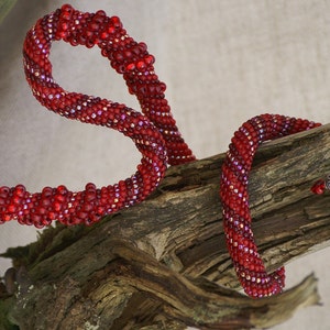 May include: A red beaded necklace with a spiral design, wrapped around a piece of driftwood.