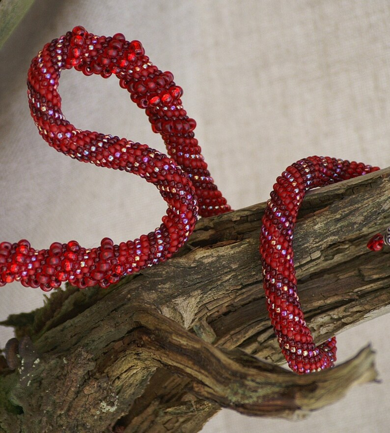 May include: A red beaded necklace with a spiral design, wrapped around a piece of driftwood.