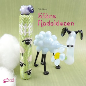 Könnte beinhalten: Ein grünes und weißes Perlennadelkissen mit einem kleinen lila und weißen Schaf oben drauf. Der Text "Sián's Nadeldosen" ist in rosa Buchstaben auf grünem Hintergrund geschrieben. Im Hintergrund befinden sich eine weiße Schaf- und eine schwarz-weiße Hundefigur.