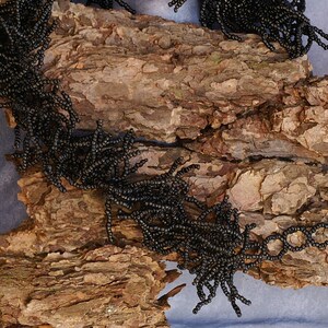 May include: Black beaded jewelry with a fringe design, displayed on a piece of tree bark.