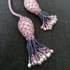 May include: A pair of beaded earrings with pink and purple beads. The earrings are shaped like teardrops and have a tassel of beads hanging from the bottom.