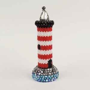 May include: A red and white striped lighthouse with a black band and a crystal top. The base of the lighthouse is covered in blue and clear rhinestones.