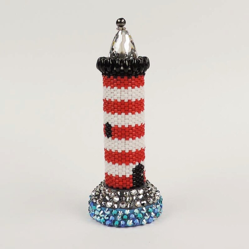 May include: A red and white striped lighthouse with a black band and a crystal top. The base of the lighthouse is covered in blue and clear rhinestones.