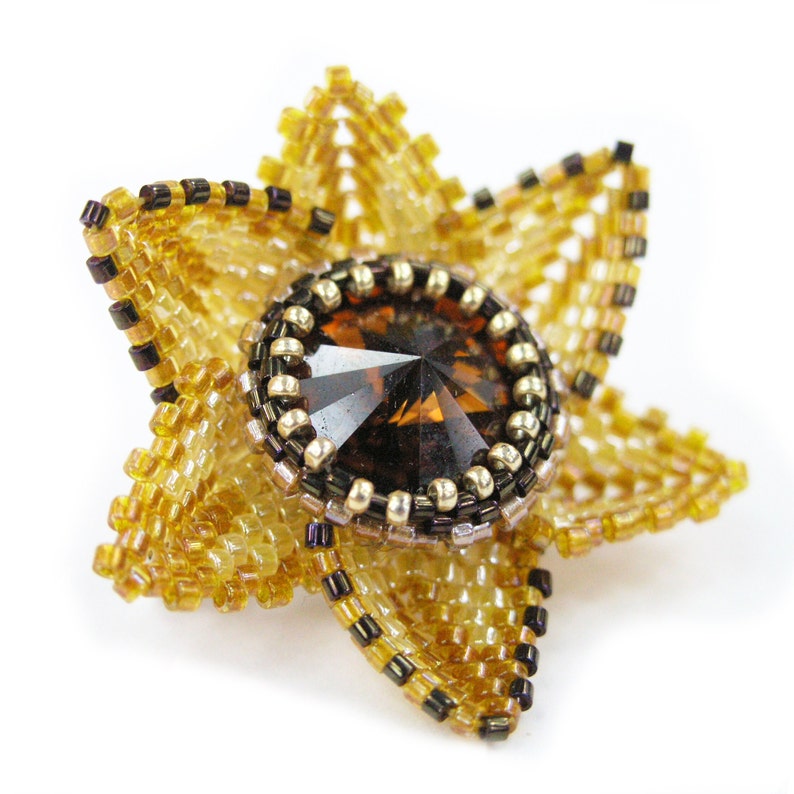 Puede incluir: Un broche de flor de cuentas doradas y marrones con una gran piedra preciosa facetada de color &aacute;mbar en el centro.