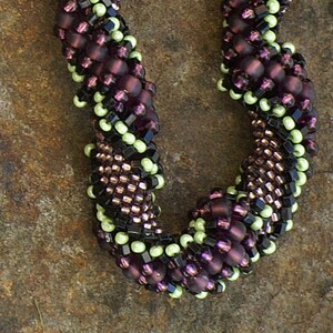May include: A close-up of a beaded necklace with a spiral design. The beads are in shades of purple, black, and green.