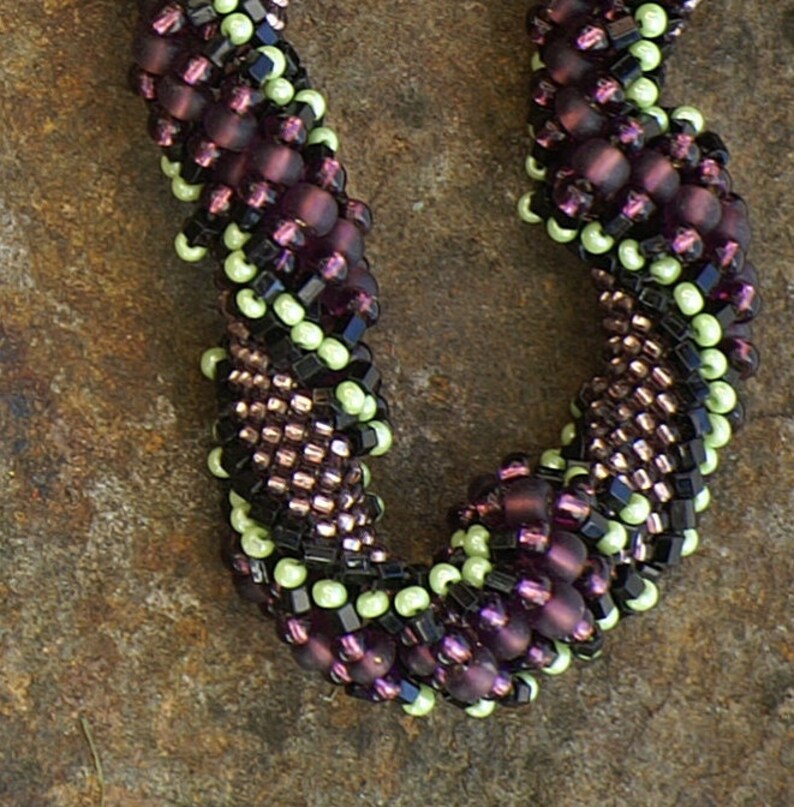 May include: A close-up of a beaded necklace with a spiral design. The beads are in shades of purple, black, and green.