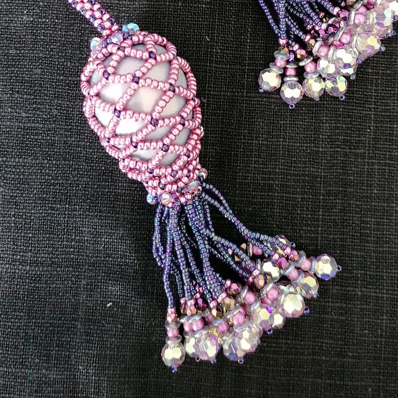 May include: A beaded necklace with a pink and purple tassel. The tassel is made of small beads and has a delicate, feminine look.