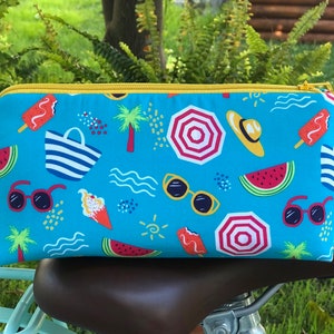 May include: A blue zippered pouch with a summer-themed print. The print features watermelons, palm trees, sunglasses, ice pops, beach umbrellas, and waves. The pouch has a yellow zipper.