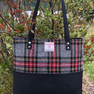 May include: A black tote bag with black leather straps and a red, black, and gray plaid fabric lining. The fabric lining has a label that reads "Harris Tweed" with a logo and the text "HANDWOVEN TWEED 100% PURE NEW WOOL MADE IN SCOTLAND".