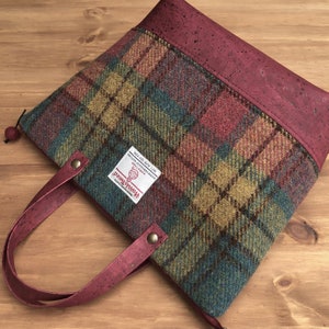 May include: A red and green plaid tote bag with a cork handle and a burgundy cork trim. The bag has a zipper closure and a label that reads "100% Pure New Wool, Made in Scotland, Harris Tweed, Handwoven, Registered Trade Mark".