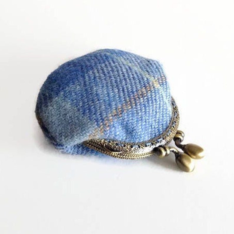 May include: A small, blue tweed coin purse with a decorative metal clasp. The purse is made of a woven blue fabric with hints of gold and brown. The clasp is ornate with two teardrop-shaped closures.