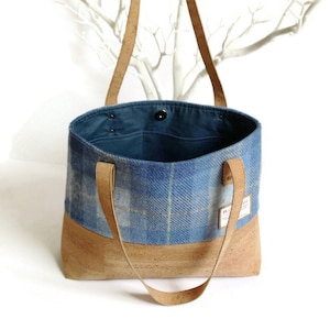 May include: A blue and white plaid tote bag with cork bottom and leather straps. The bag has a blue cotton lining and a small pocket inside.