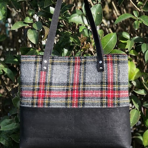 May include: A black and gray plaid tote bag with a black leather bottom. The bag has black leather straps.