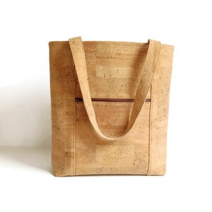 May include: A large, light brown cork tote bag with two long straps. The bag has a zippered pocket on the front.