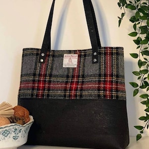 May include: A black tote bag with black straps and a red, black, and gray plaid pattern. The bag has a label that says "Harris Tweed" and "100% Pure New Wool".