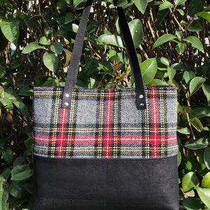 May include: A black tote bag with black leather straps and a plaid pattern in red, yellow, and gray. The bottom half of the bag is black.