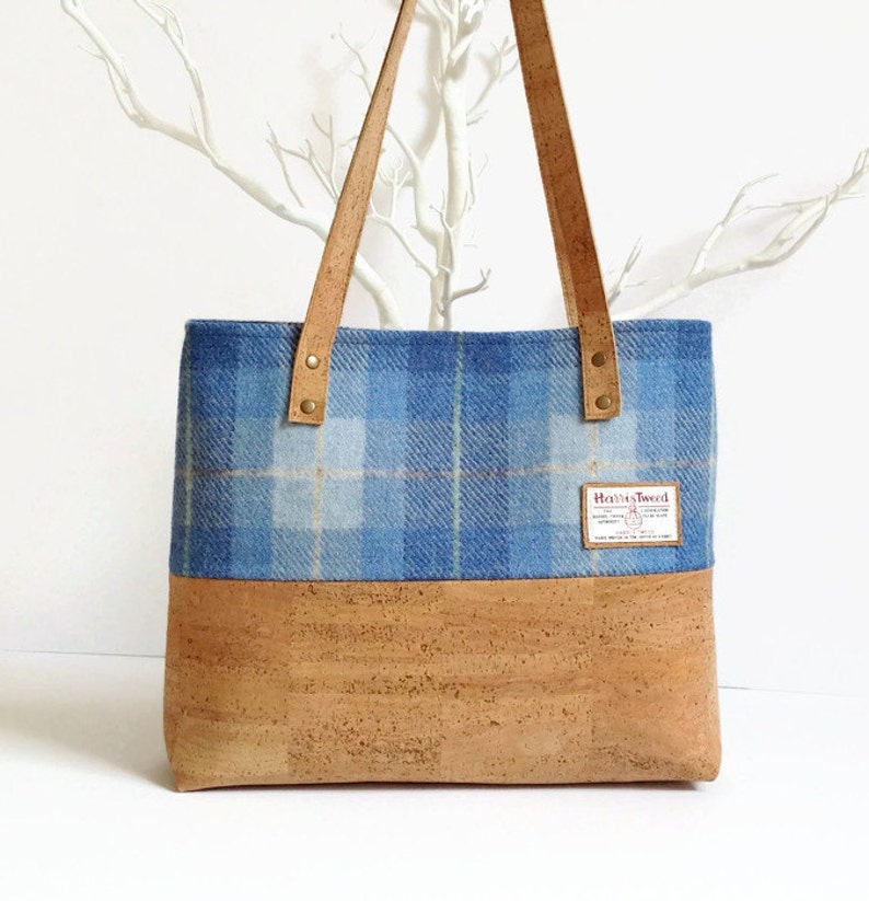 May include: A blue and white plaid tote bag with a cork bottom and leather straps. The bag has a label that says "Harris Tweed."
